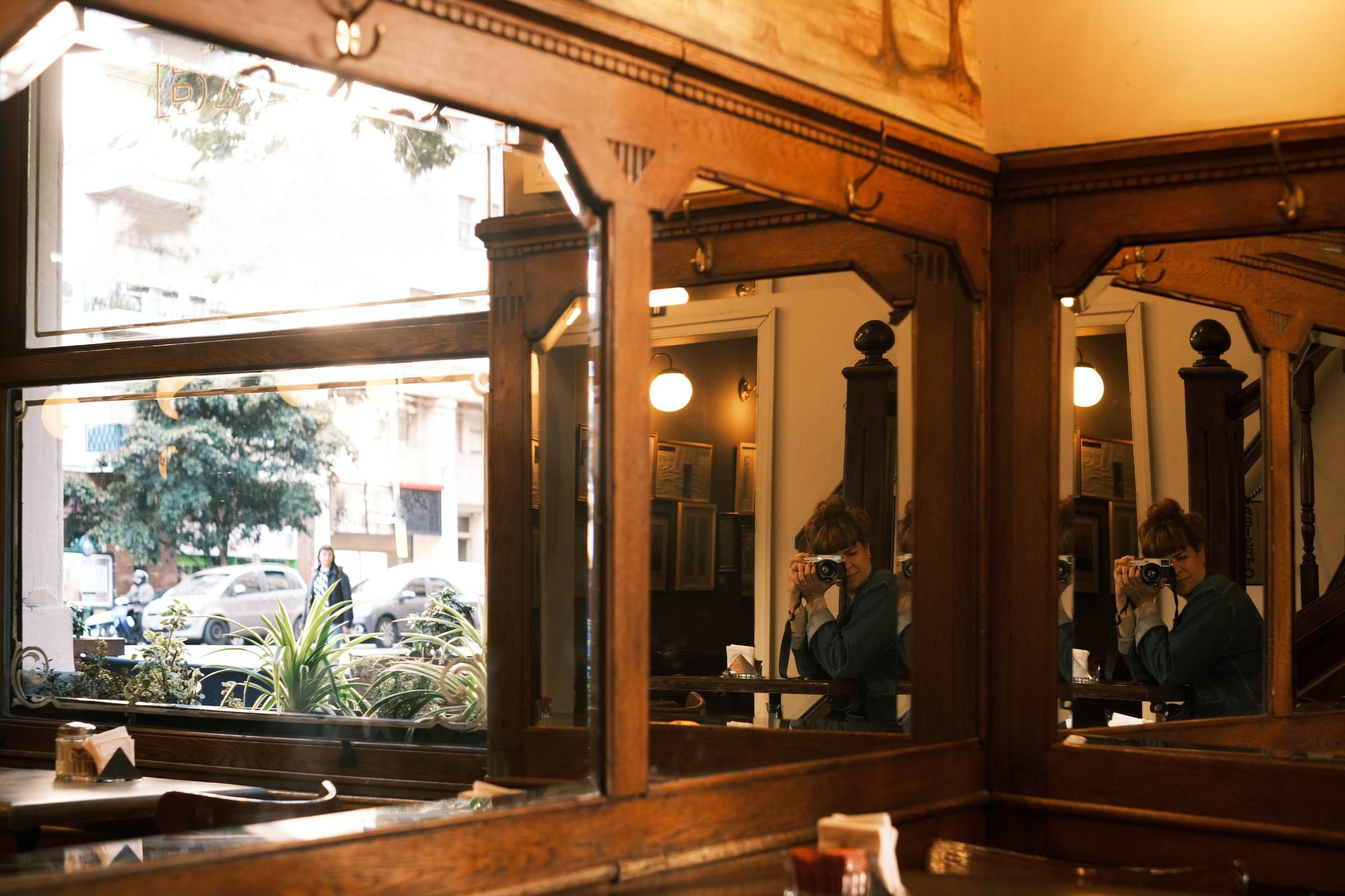 Reflections of a photographer in a traditional cafe in the city of Buenos Aires. Views of the street and anonymous passer-bys through the window. Vintage style decor and mirror.