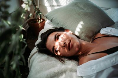 A person sitting by a window with sunlight, a plant, and buildings outside.