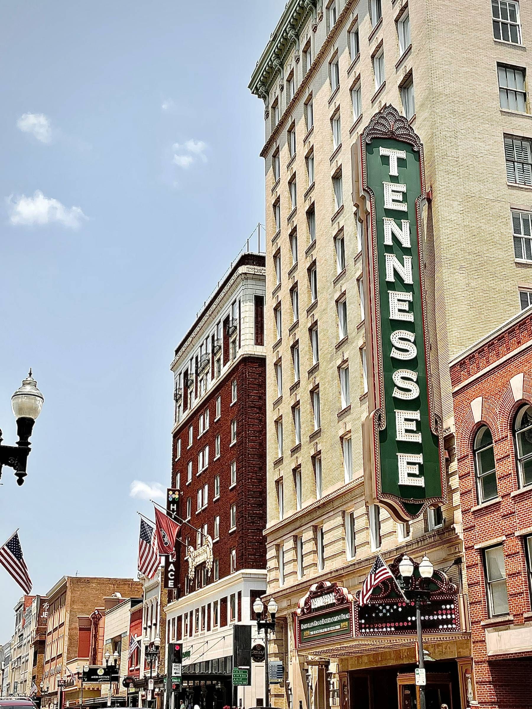Street with historic Tennessee theater sign, surrounded by vintage buildings and American flags, under a clear sky.