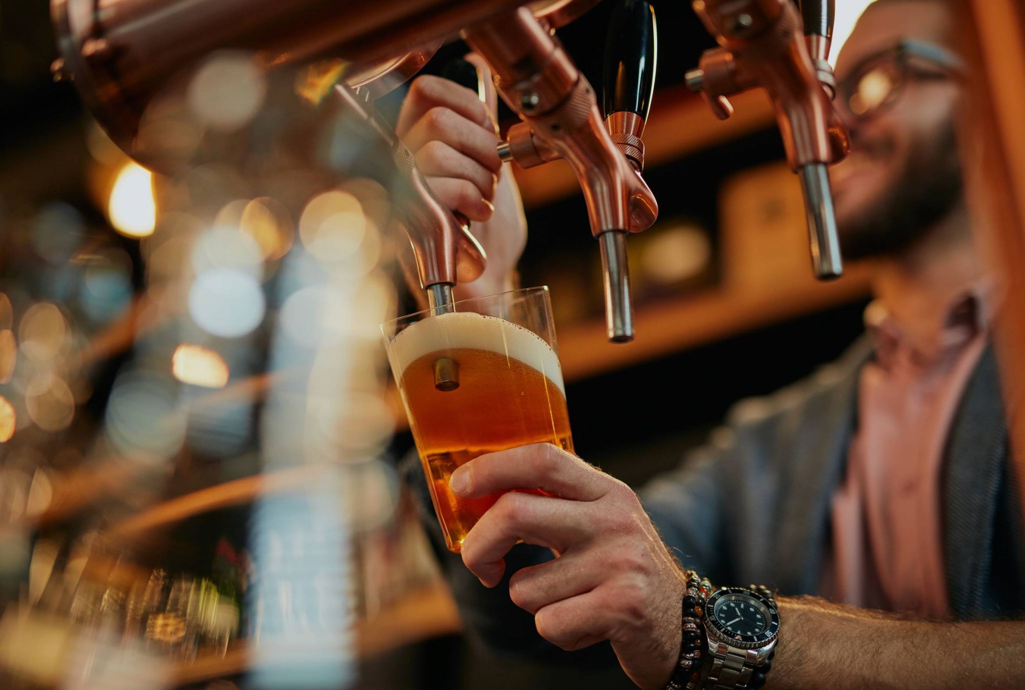 Person pouring beer from a tap into a glass, creating a foamy top.