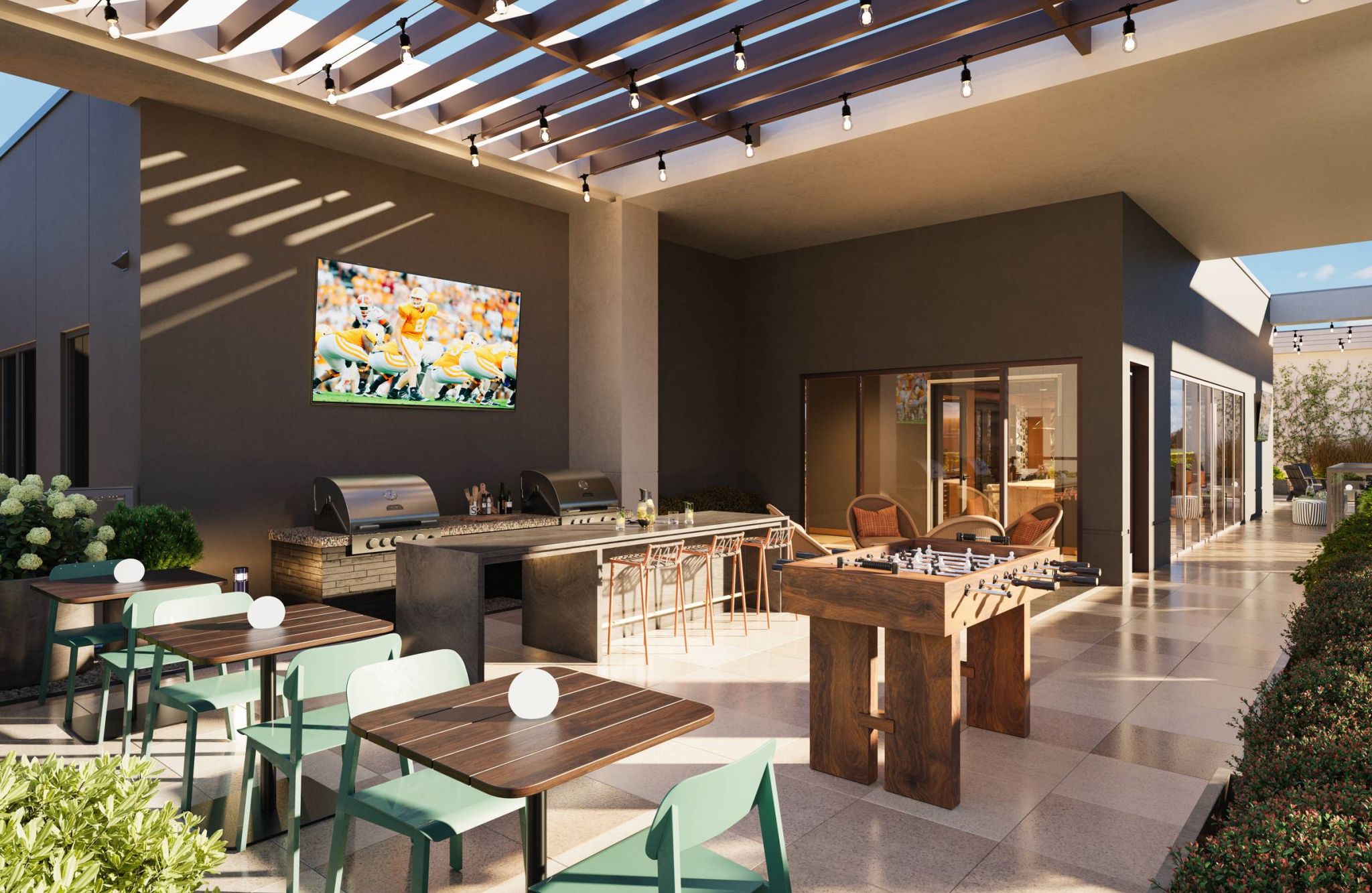 EVER Knoxville apartments Outdoor patio with dining tables, grill, foosball table, TV, and string lights under a slatted pergola.