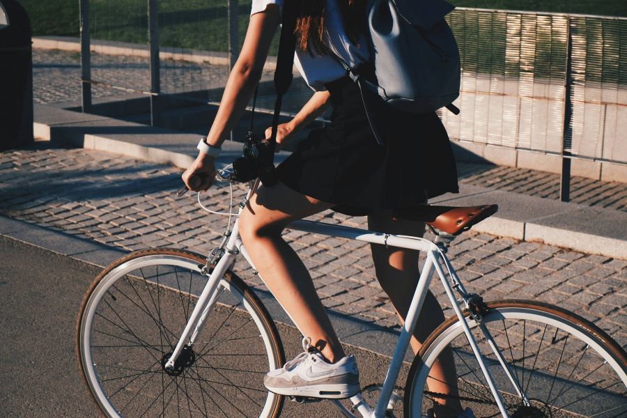 Person riding a white bicycle on a paved path, wearing a black skirt and a grey backpack.